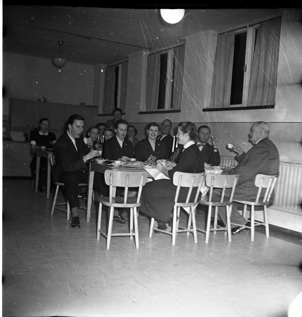 Män, kvinnor och barn sitter vid kaffebord med tända ljus. Till höger närmast väggen sitter Allan Berggren och A E Bolling.