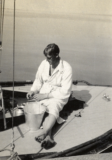 En man i badrock som skalar potatis (?) på en segelbåt.