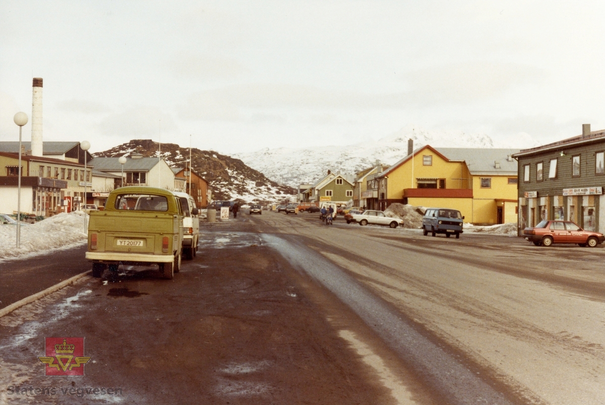 E 10. Leknes sentrum i Vestvågøy kommune. Før vegomlegging. 
Bilde 2) Biler i gaten, nærmest en 1976 modell  Volkswagen VW 26-16.