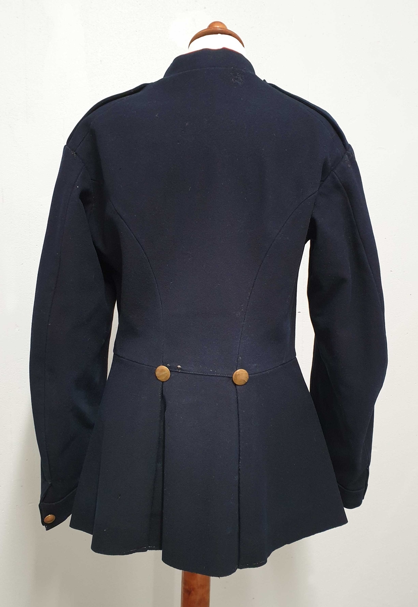 Mørkeblå uniform bestående av jakke og bukse. Jakken er enkeltspent, med messingknapper foran og på mansjettene. Rød kant på kragen. 4-tall på skulder