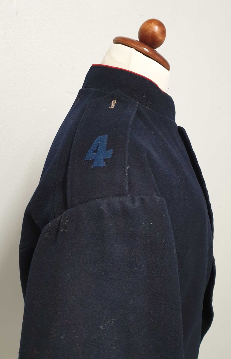 Mørkeblå uniform bestående av jakke og bukse. Jakken er enkeltspent, med messingknapper foran og på mansjettene. Rød kant på kragen. 4-tall på skulder
