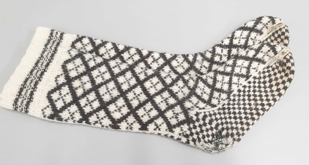 Ett par håndstrikkede ullstrømper, med mønster i svart og hvitt.