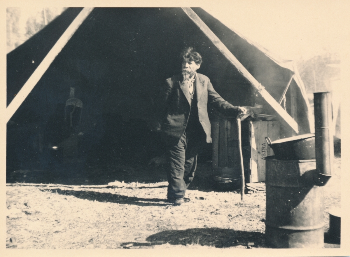 En äldre man stöder sig mot en käpp, stående framför ett tält. Bilden är troligen tagen i samband med marknaden i Torsby.