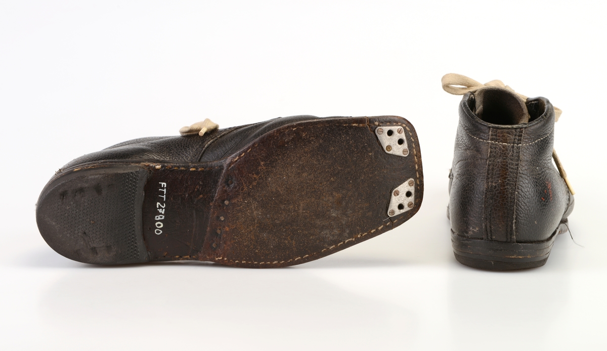 Et par dameskisko i svart skinn. Skoene er randsydde og har såler av skinn og hæler av gummi. I front er det 6 par metallmaljer for snøring. Under snøringen er det en enkel skinntunge. Skoene er snøret med hvite skolisser. Inenrsålen er av tre og på hælområdet er det limt på svart skinn. Kanten oppe på skoen er polstret. Foran på undersiden av skoen er det to hull på hver side. Det er jernbeslag rundt hullene for feste i tåbindinger.