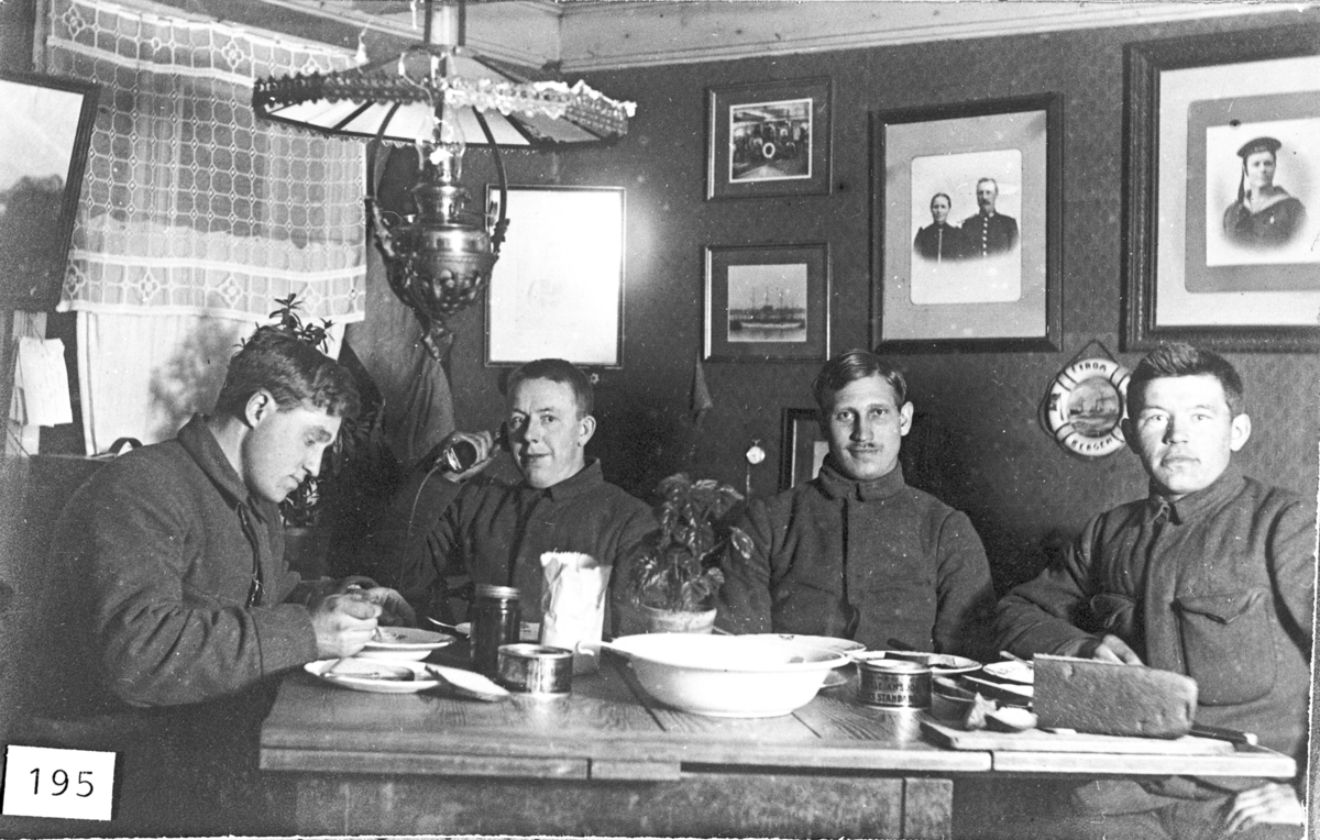 Menn på nøytralitetsvakt ca. 1918. Interiør med bilder på vegg, parafinlampe. 
