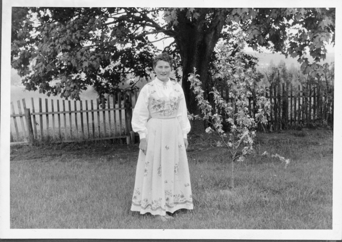 Kvinne i Lundebybunad i hage med blomstrende epletre, trolig etter andre verdenskrig.