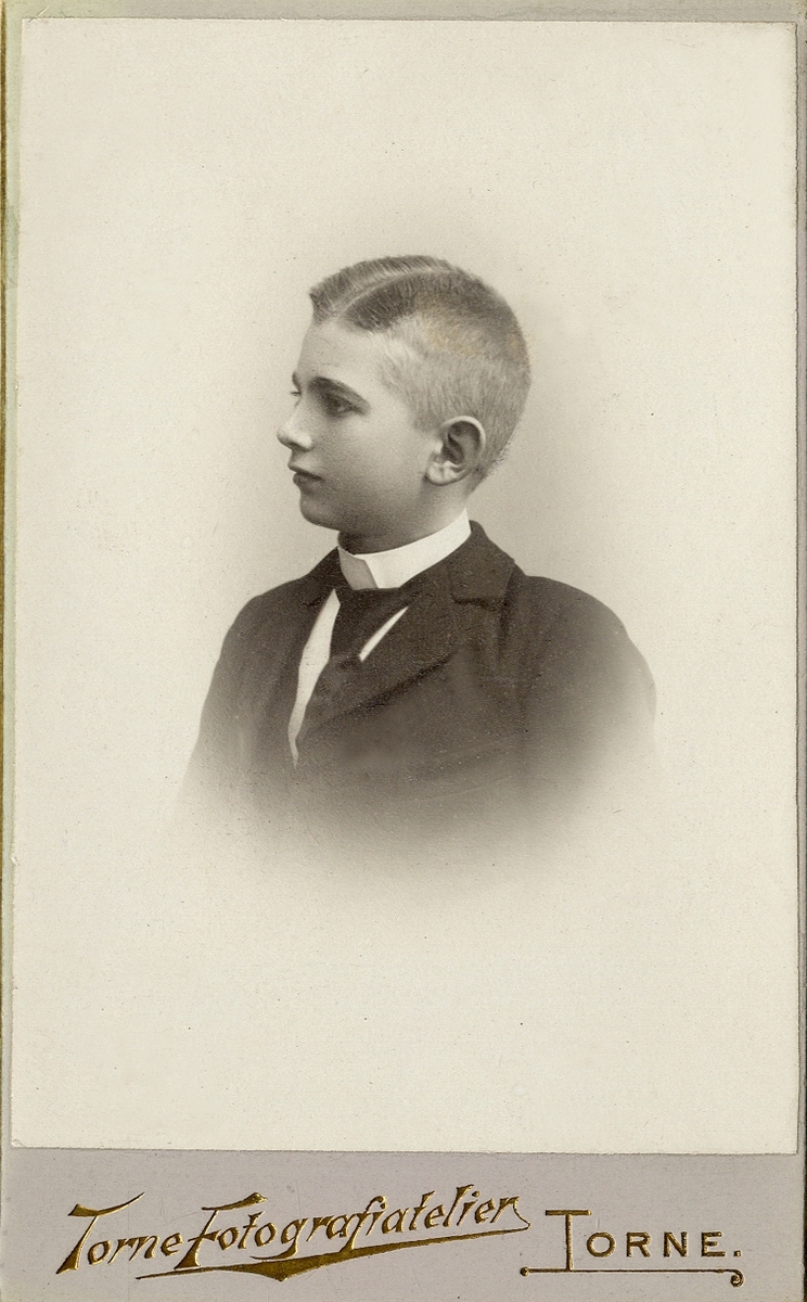 Porträttfoto av en ung man i mörk kavajkostym med stärkkrage och slips. 
Bröstbild, halvprofil. Ateljéfoto.