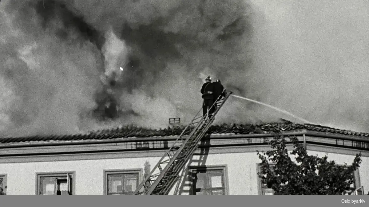 Det brenner fra taket på en bygning på St. Olavs plass. Brannmenn holder på å slukke brannen.