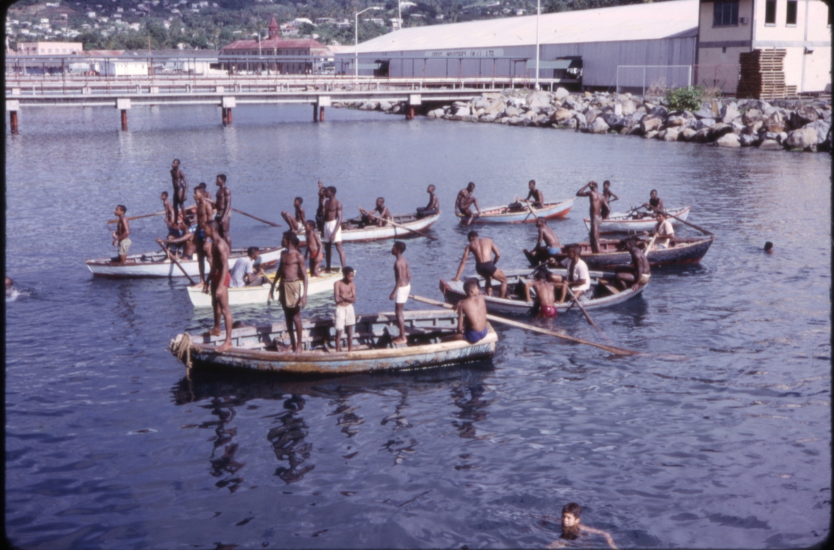Unge menn i småbåter bader like ved industriområde. 'Sagafjord' Christmas Holiday Cruise 1965.
