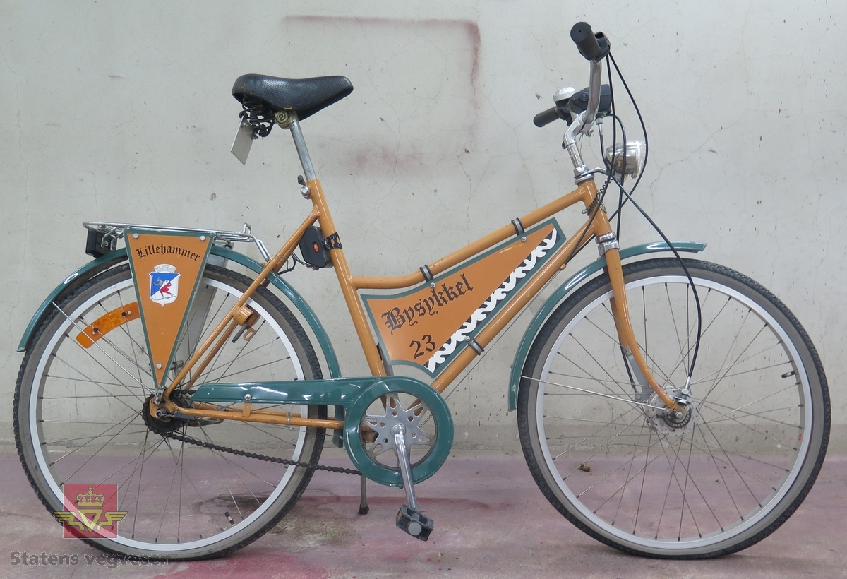 DBS damesykkel. Sykkelen har oransje ramme og grønn kjedekasse og skjermer. Utstyrt med lykt foran, og speedometer. Har 5 gir (type Torpedo).