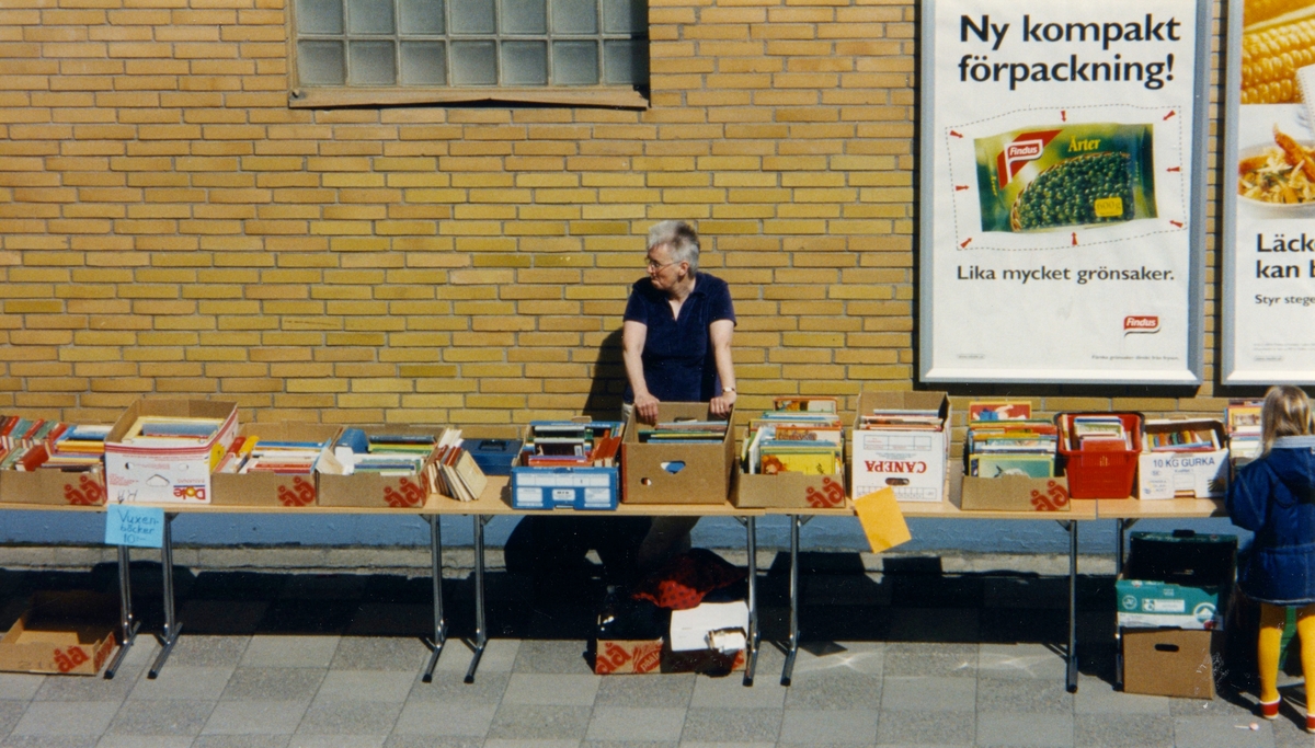Bibliotekschef Ingalill Ekwall har bokutförsäljning för Kållereds bibliotek på inre torget i Kållereds centrum, cirka år 2000. I bakgrunden ses den gula tegelväggen till Bonum (senare Netto, Coop och Vårdcentral).
