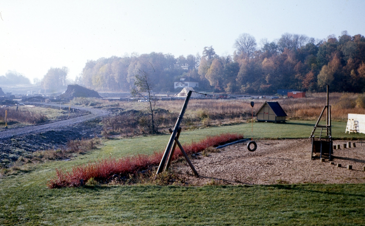 Högenvägen läggs ut vid sidan av lekplatsen i Vommedal, cirka 1975. I mitten Glimskogs hus. I bakgrunden ses kyrkskogen.