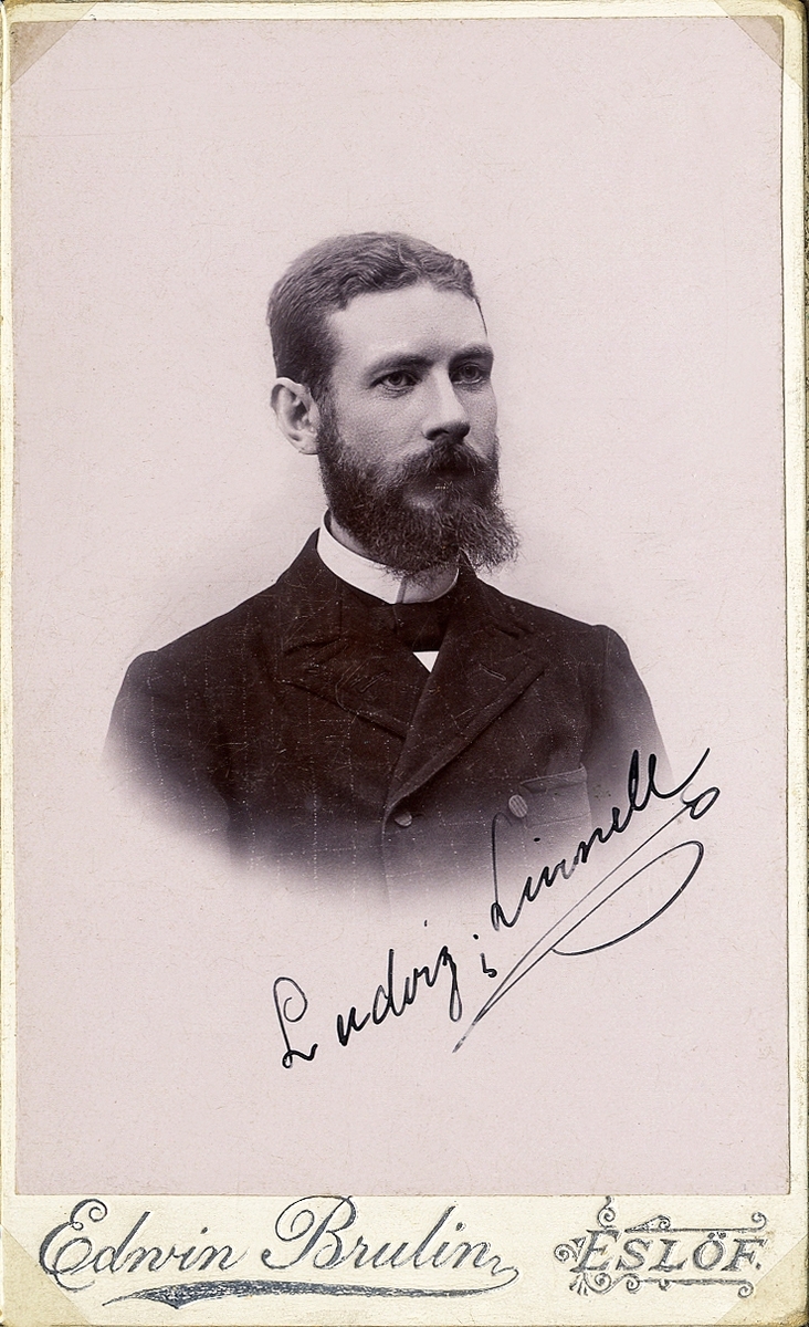 Foto av en man med helskägg, klädd i mörk, rutig kavajkostym med stärkkrage och fluga. 
Under fotot syns en autograf: "Ludvig Linnell". 
Bröstbild, halvprofil. Ateljéfoto.