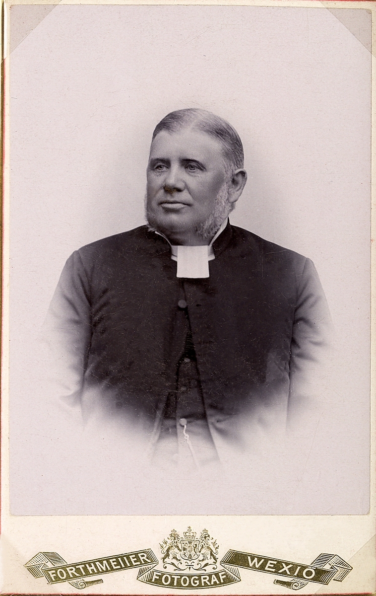 Foto av en man i prästrock och prästkrage m.m.
Knäbild, halvprofil. Ateljéfoto.