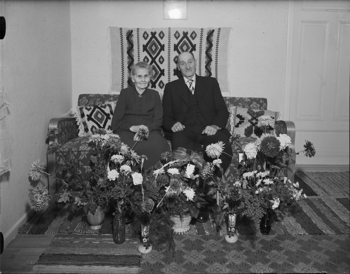 Kvinna och man omgivna av blommor i hemmiljö, Östhammar, Uppland