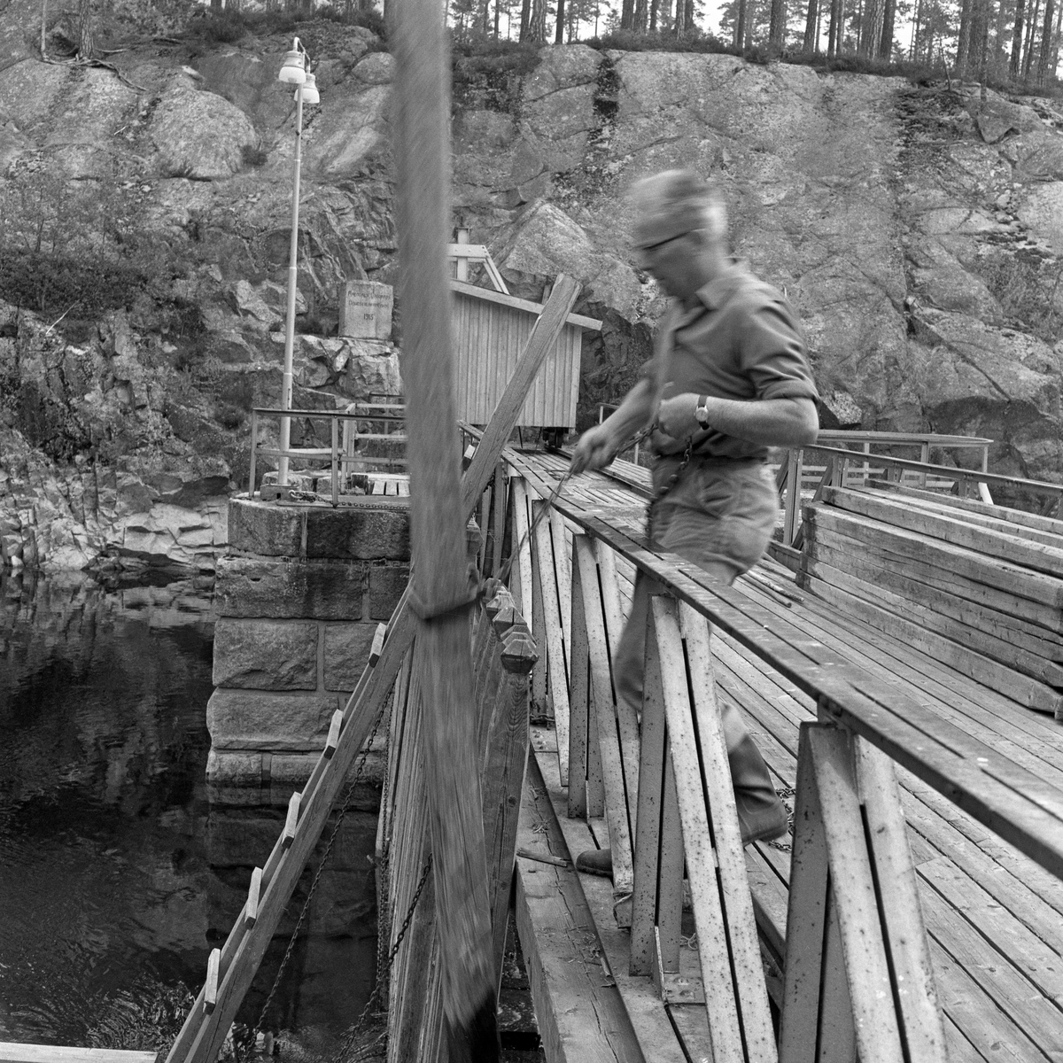 Nåledam. Nålene tas. Damredskap. Nisserdammen i Arendalsvassdraget. Nisser dam ved utløpet av innsjøen Nisser i Telemark. Damvokter Karl Hansen viser bruk av nåleklave når han tar nålene i dammen.