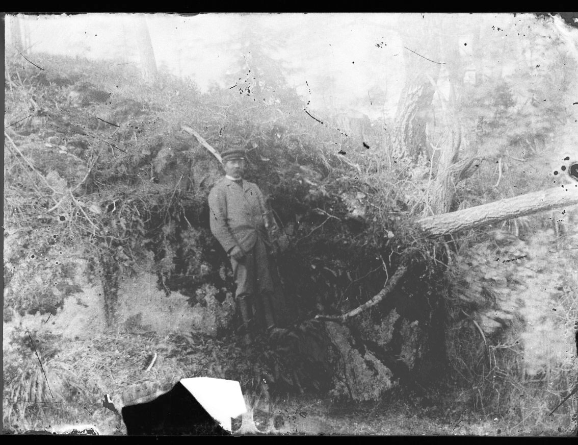 En okänd man står lutad mot en bergknalle med en rotvälta intill sig.