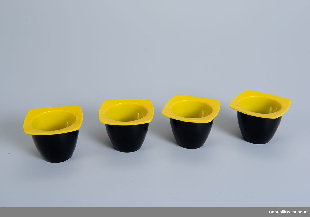 Äggkoppar av plast med fyrkantigt bräm.
Tvåfärgade, utsida svart, insda och bräm gult.
Märkning i botten: 
Jonas
DESIGN Per Bjelving
