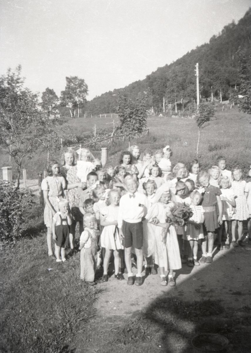 Gruppeportrett av ei stor gruppe barn der de to barna i midten er utkledd som brud og brudgom.