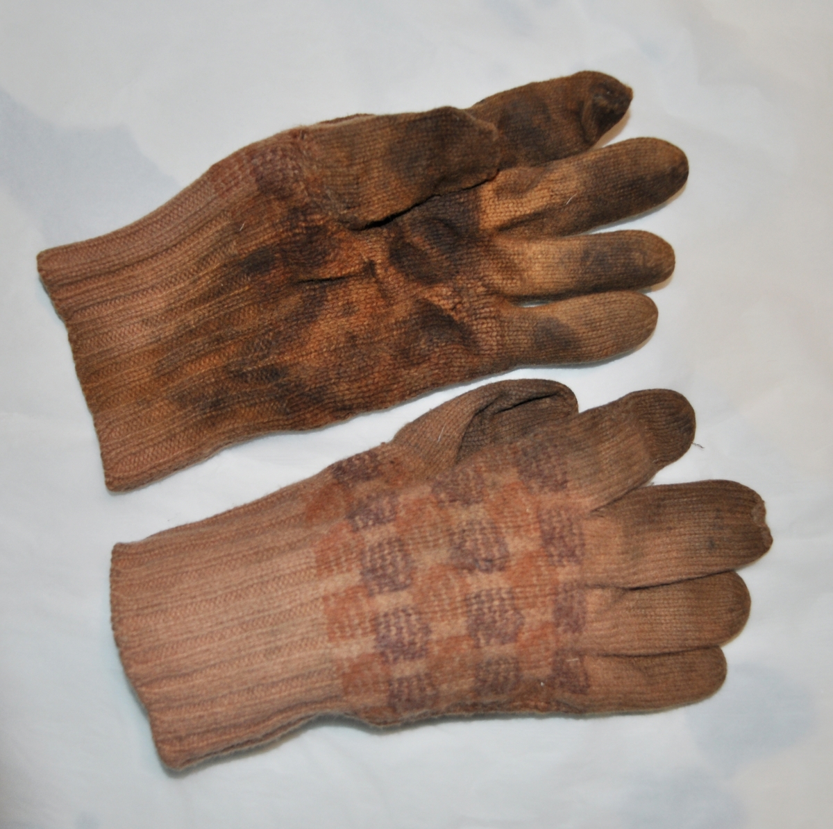 Ett par stickade fingervantar med rutor på handloven i svart. Orangbrun färg i övrigt.