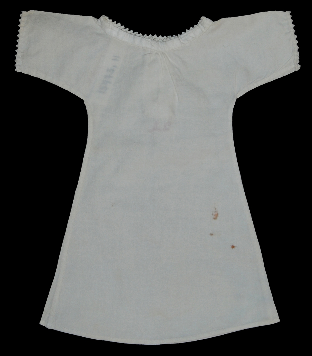 Vit nattskjorta, märkt IB, med uddspets kring hals och halsöppning, en knapp i halsen sammanhåller
skjortan, spets kring ärmarna,