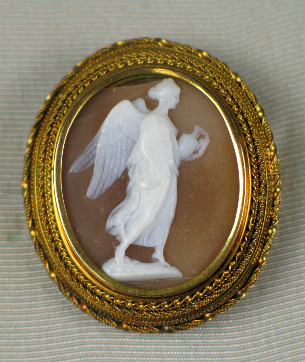Kamè/medaljong innfattet gull som består av sirlige filigransborder. I midten en utskåret hvit engel som bærer en krukke.