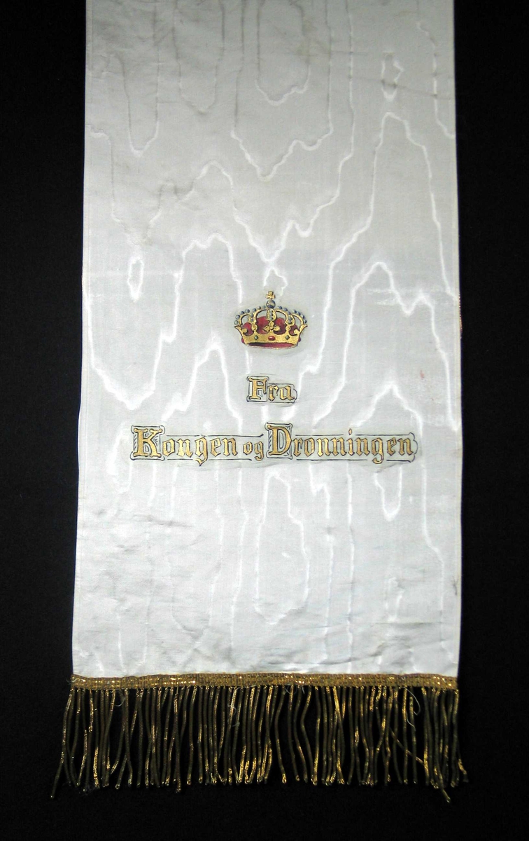 Begravelsessløyfe i hvit silke med frynser og tekst i gull.