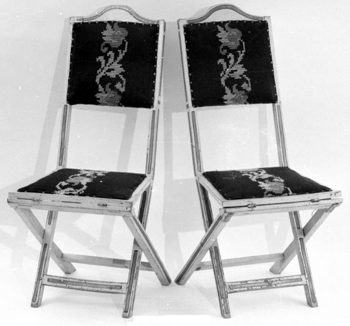Stolene er av tre, laget slik at det er mulig å slå dem sammen. Stoltrekket er mørkerødt brodert tekstil, som er naglet fast. Stolene er grå med svart og gulllignende dekor.