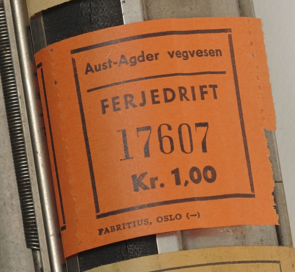 Billettholder, fra ferge.  Forkrommet metall, fabrikkstempel: Fabritius. Sylinder, med 6 ruller billetter,  gradert fra kr. 0,10 til kr. 1,50.