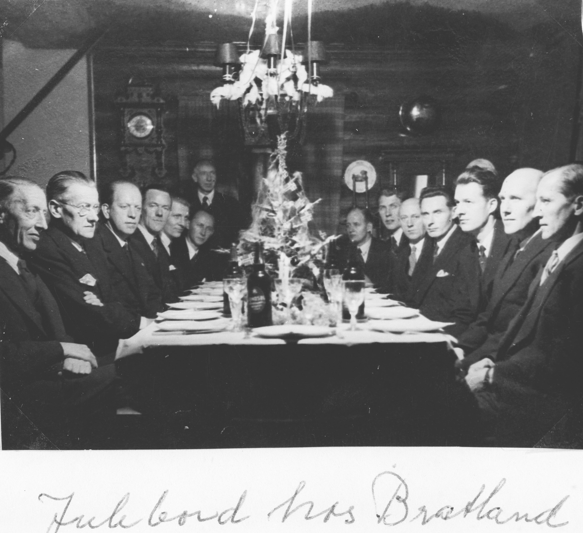 Gruppeportrett av 15 menn, sittende rundt et bord. Bratlandkvartetten på jJulebord hos Bratland.