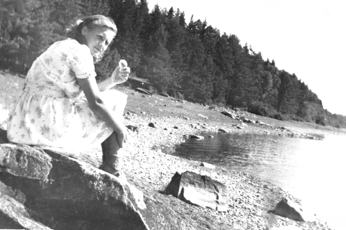 Anna Hatterud f.1931 sitter på stranda ved Furusetstua på Trosterud, Helgøya.