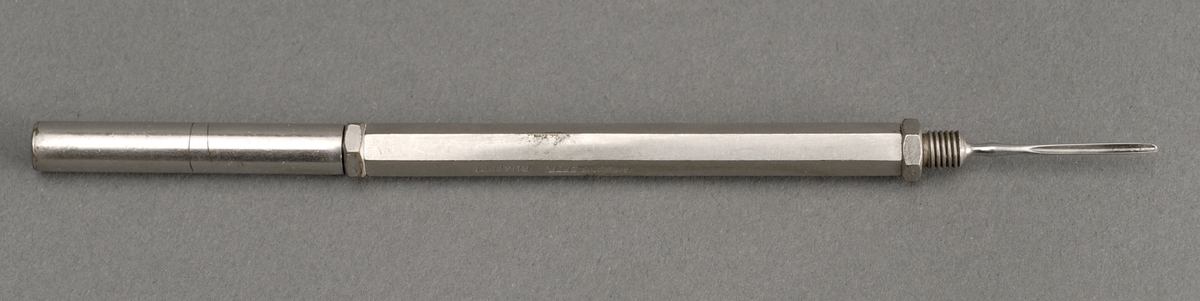 6 kantet metallholder med corneaskrape og liten kniv, skalpell, i hver sin ende. Beskyttelselokk med skru i den  ene enden.