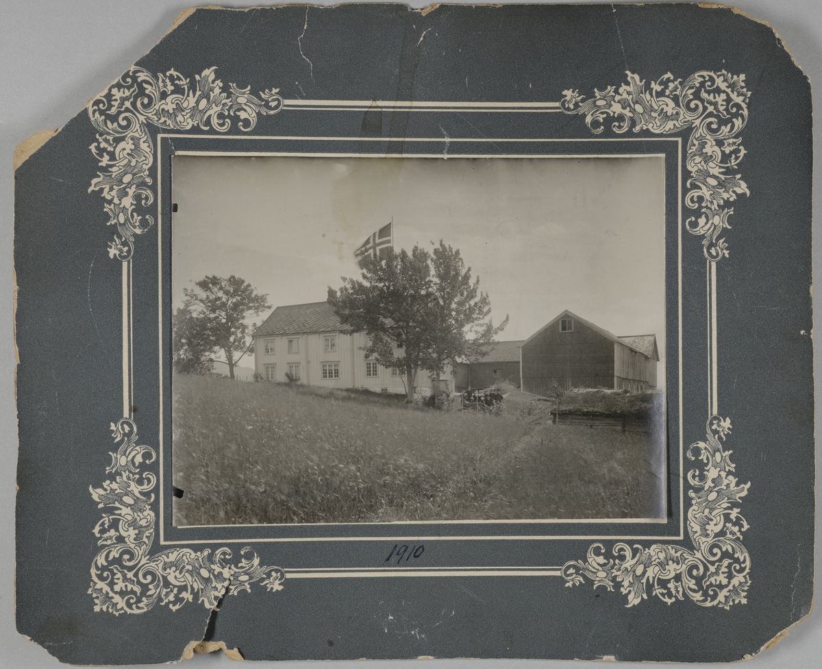Svart-hvitt fotografi av Klæt gård, vestre. Fotografiet er montert på en grå papplate med organisk dekor i hjørnene av en illudert ramme.