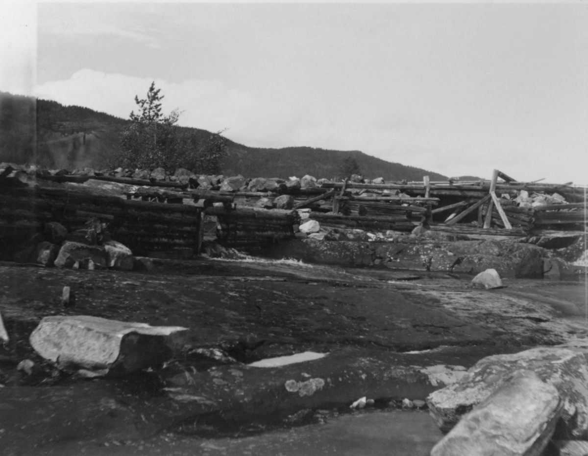 Øvre Bjorvassdam eller Bjørvassdam i Rauavassdraget i Tinn i Telemark.  Fotografiet skal være tatt i 1937, i motstrøms retning.  Vi ser ei rekke av steinfylte tømmerkiser som er reist på en relativt slak bergrygg med enkelte steinblokker.  Den sinklaftete konstruksjonen later til å været i ferd med å svikte, antakelig på grunn av råte i tømmerkonstruksjonene, som antakelig hadde ligget under åpen himmel i mange tiår. 