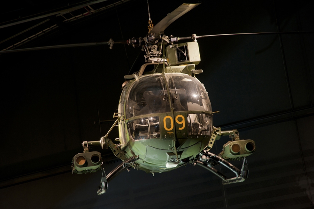 Helikopter, Hkp 9A. 
MBB BO 105 CB3

Kamouflagemålad attackhelikopter, utrustad med två turbinmotorer. Längst med sidorna sitter medar. Beväpnad med fyra robotkapslar. Tvåsitsig. Ovanför huv sitter siktesinstallation. Fyrbladig rotorinstallation på ovansidan samt mindre tvåbladig rotor på fena.
Märkning: Kodsiffra 09 fram och på sidan, kronmärke på bakkroppen samt bak sitter texten Försvarsmakten.