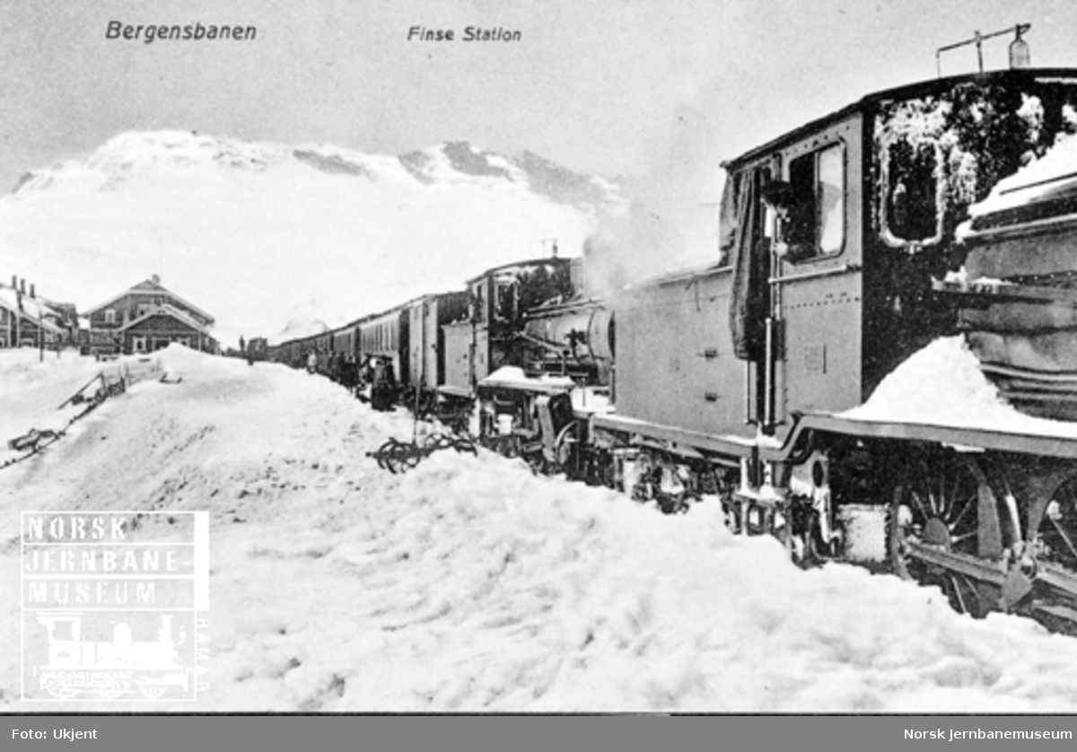 Vinterbilde fra Finse stasjon med østgående persontog trukket av to damplokomotiver av type 18 i spor 1