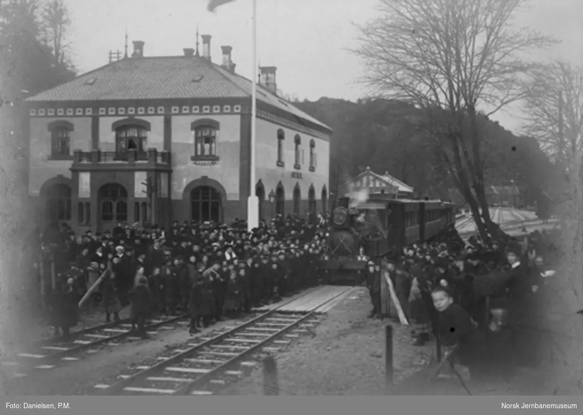 Åpningstoget ved returen til Arendal stasjon, trolig ved åpningen til Froland 23. november 1908 : stor folkemengde på stasjonen, hvor lokomotivstall og verksted er under bygging i bakgrunnen