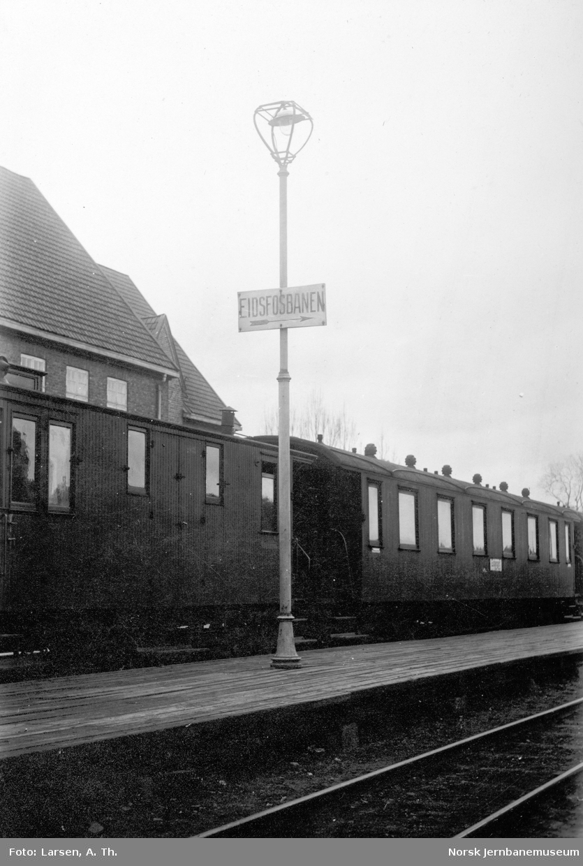 Plattformen på Tønsberg stasjon med skilt "Eidsfosbanen" og tog i spor 1