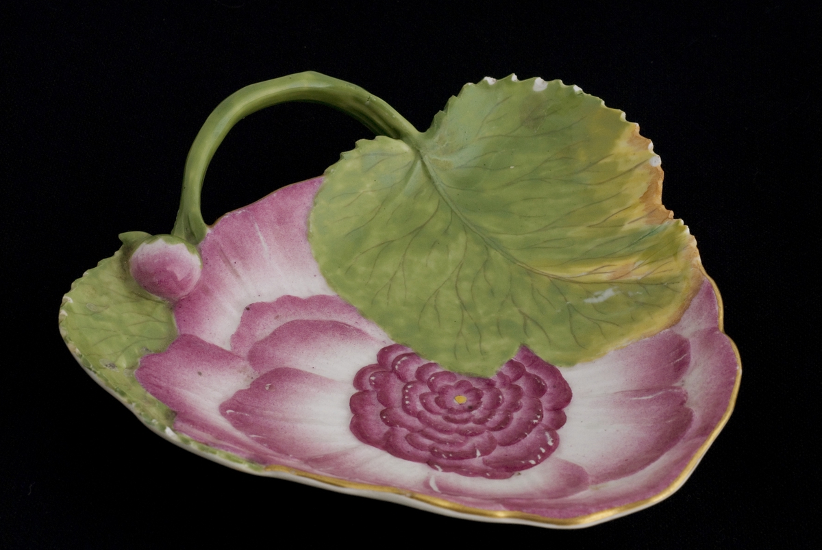 Tresidet porselensskål, dannet av en rød blomst, to grønne blad, hanken en stilk. Merket med to kryssede sverd
