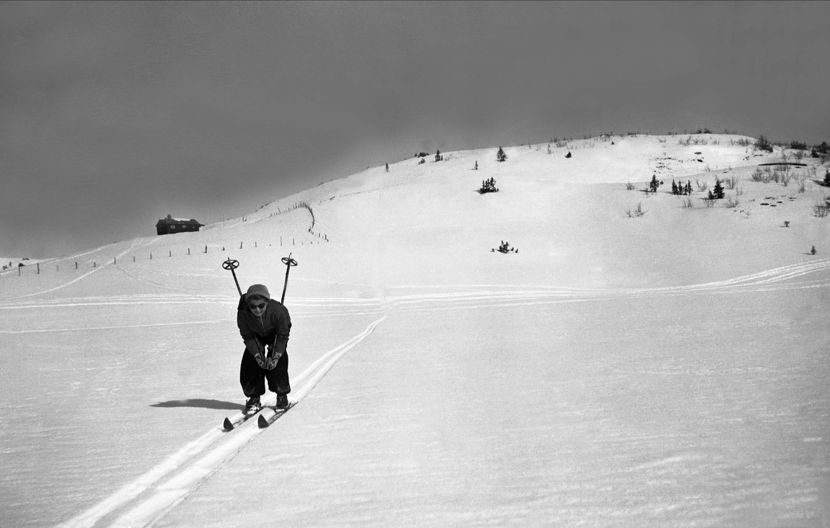 Kvinne i skiløypa, landskap med hytte i bakgrunn. Fotografert påsken 1940.