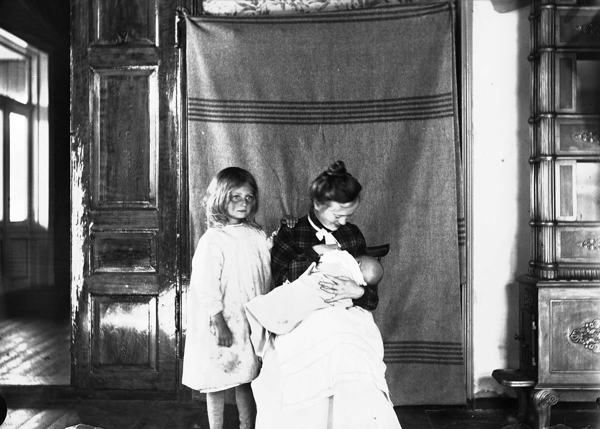 Interiør, Nedre Digerud, Frogn, Akershus, 1902. Gudrun og Margrethe med Halvor Nicolai Q. Wiborg, fotografert foran opphengt bakteppe.