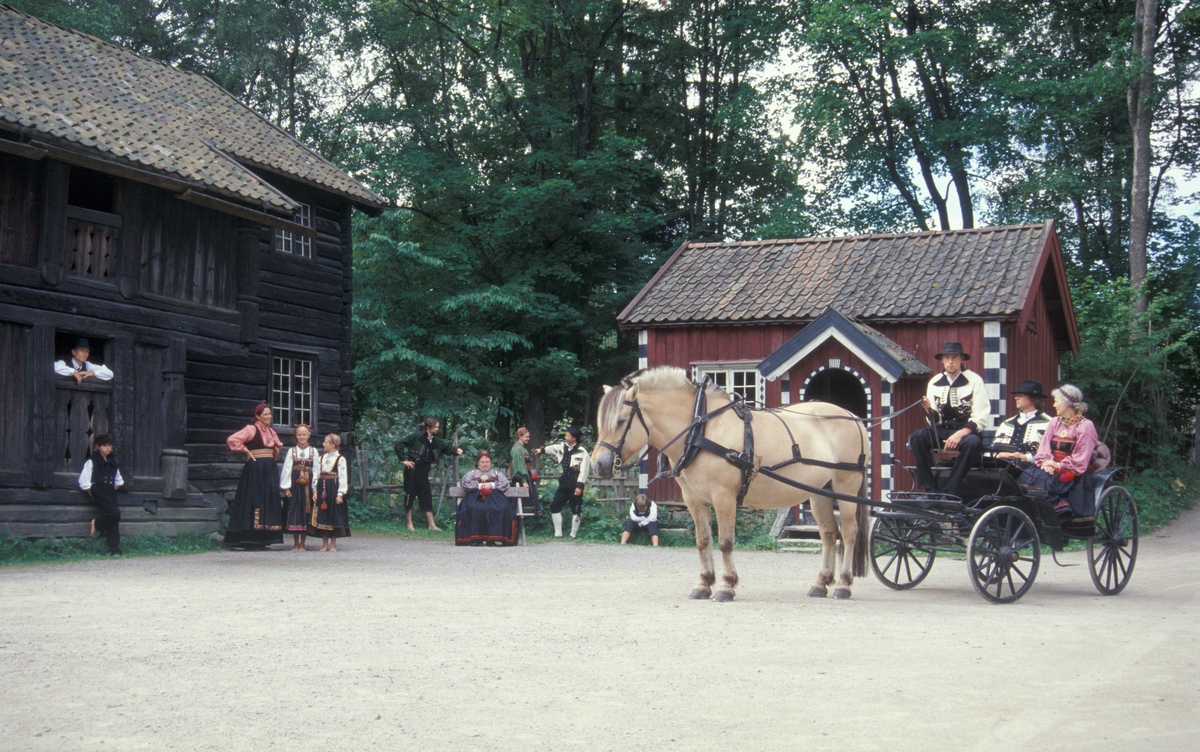 Verter i drakter på Telemarkstunet, Norsk Folkemuseum. Hest og vogn foran Cappelenstua, bygning nummer 132 og Ylistua, bygning nummer131.