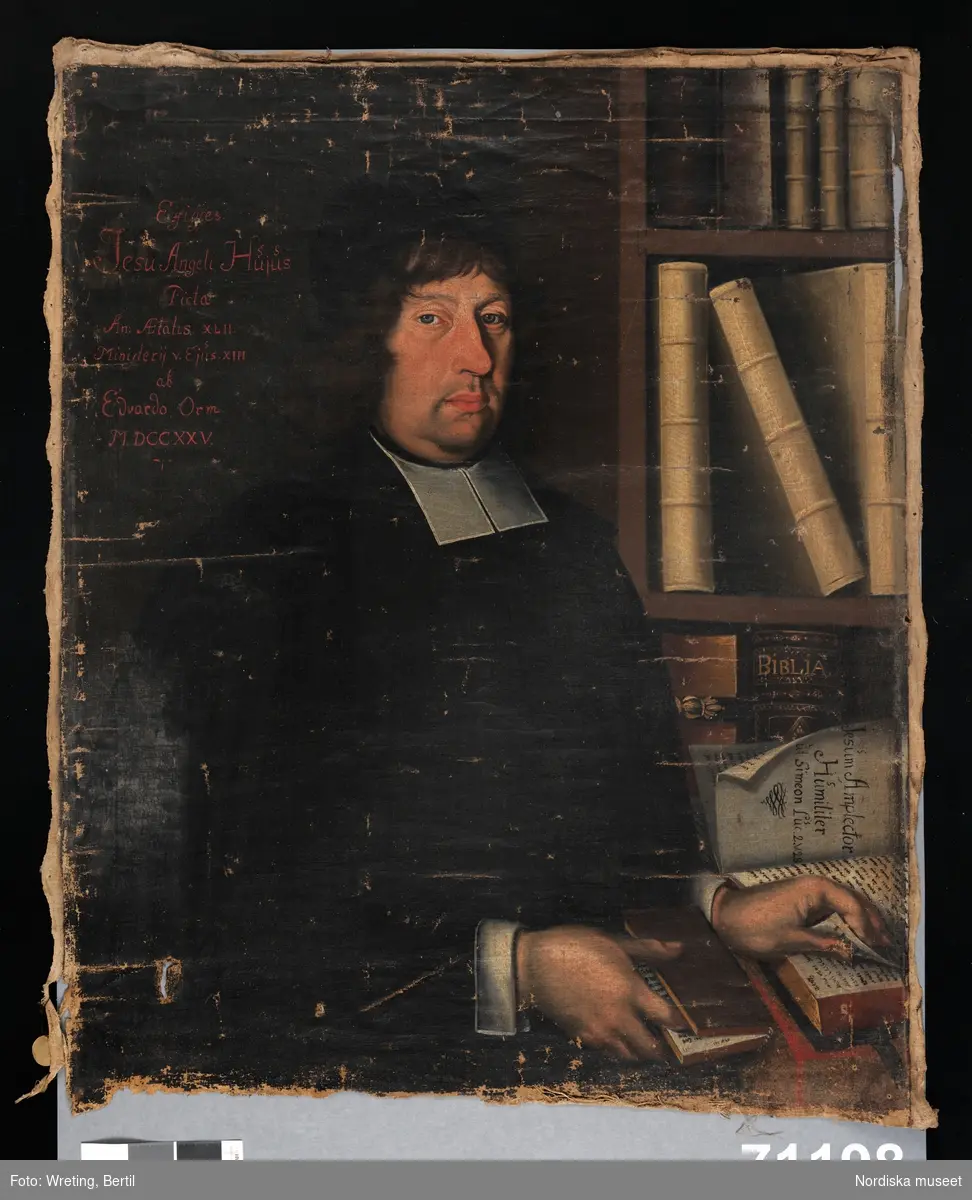 Prästporträtt, midjebild, vänt åt vänster placerad framför bokhylla. Blicken möter betraktarens, båda händerna bläddrar/håller i böcker.