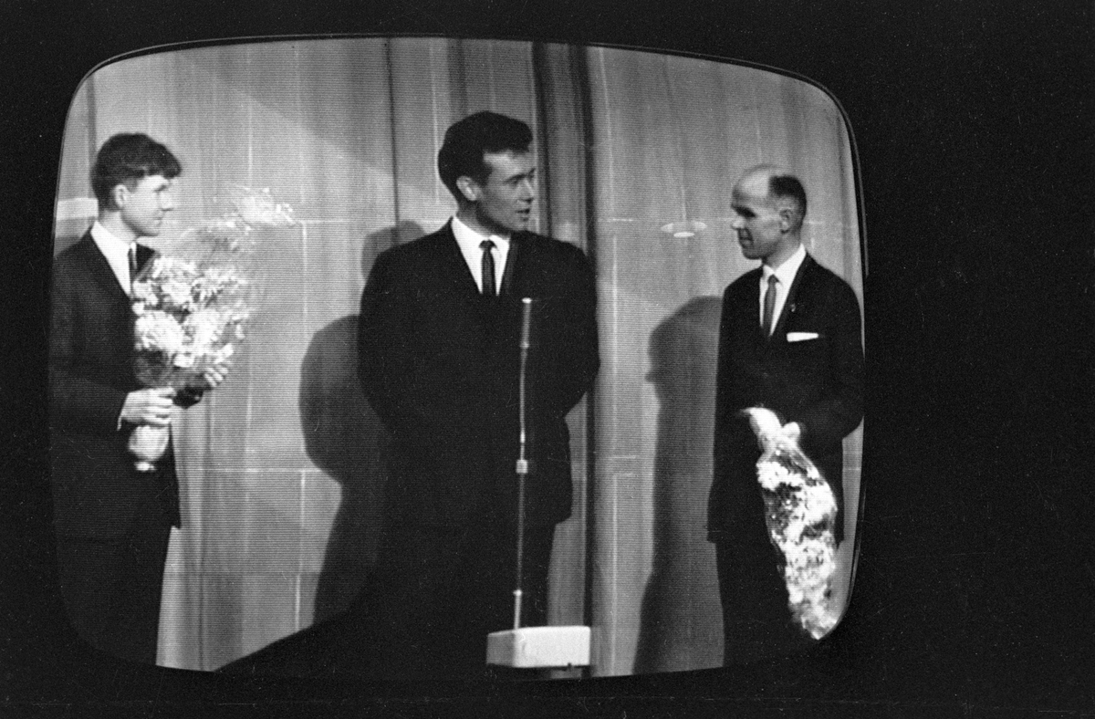 Fra NRKs fjernsynsprogram "Kvitt eller dobbelt"  i oktober 1966. Programleder Knut Bjørnsen i midten sammen med to av deltakerne som har fått hver sin blomstebukett. Avfotografert fra fjernsynet.