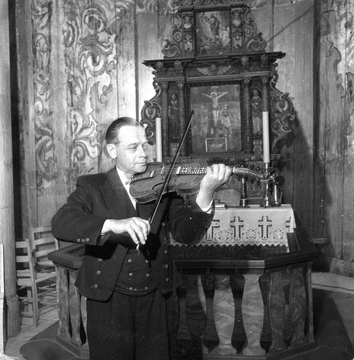Gjermund Haugen spiller hardingfele ved altertavlen i Heddal stavkirke, Notodden. Fotografert juni 1958.