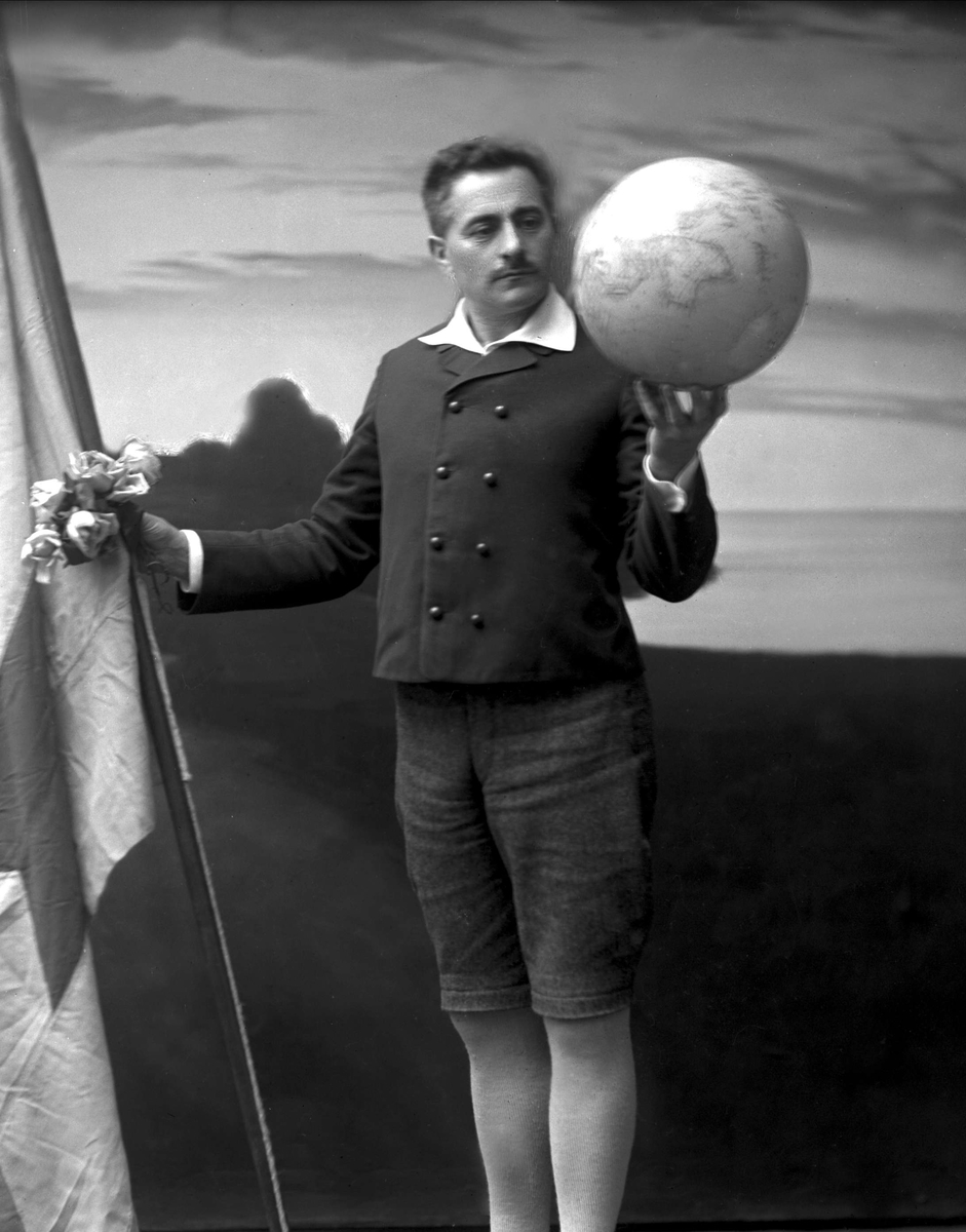 Portrett av Sigert Patursson med knebukser og mørk jakke. Holder en globus i ei hånd og en fane/flagg i andre hånd. Redaktør Paturson. Færøysk flagg, antakelig.