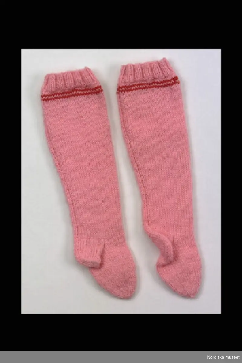 Inventering Sesam 1996-1999:
L 9 cm (strumpa b.)
L 18 cm (strumpa a.)
Två par strumpor till docka, av stickat rosa bomullsgarn. Strumpa a) har en röd rand vid resåren. 
Helena Carlsson 1996