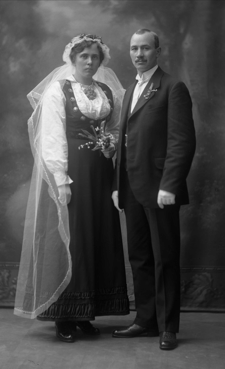 Gruppebilde, bryllupspar. Han i dress, bruden i folkedrakt fra (Øst-)Telemark, med hvitt brudeslør.