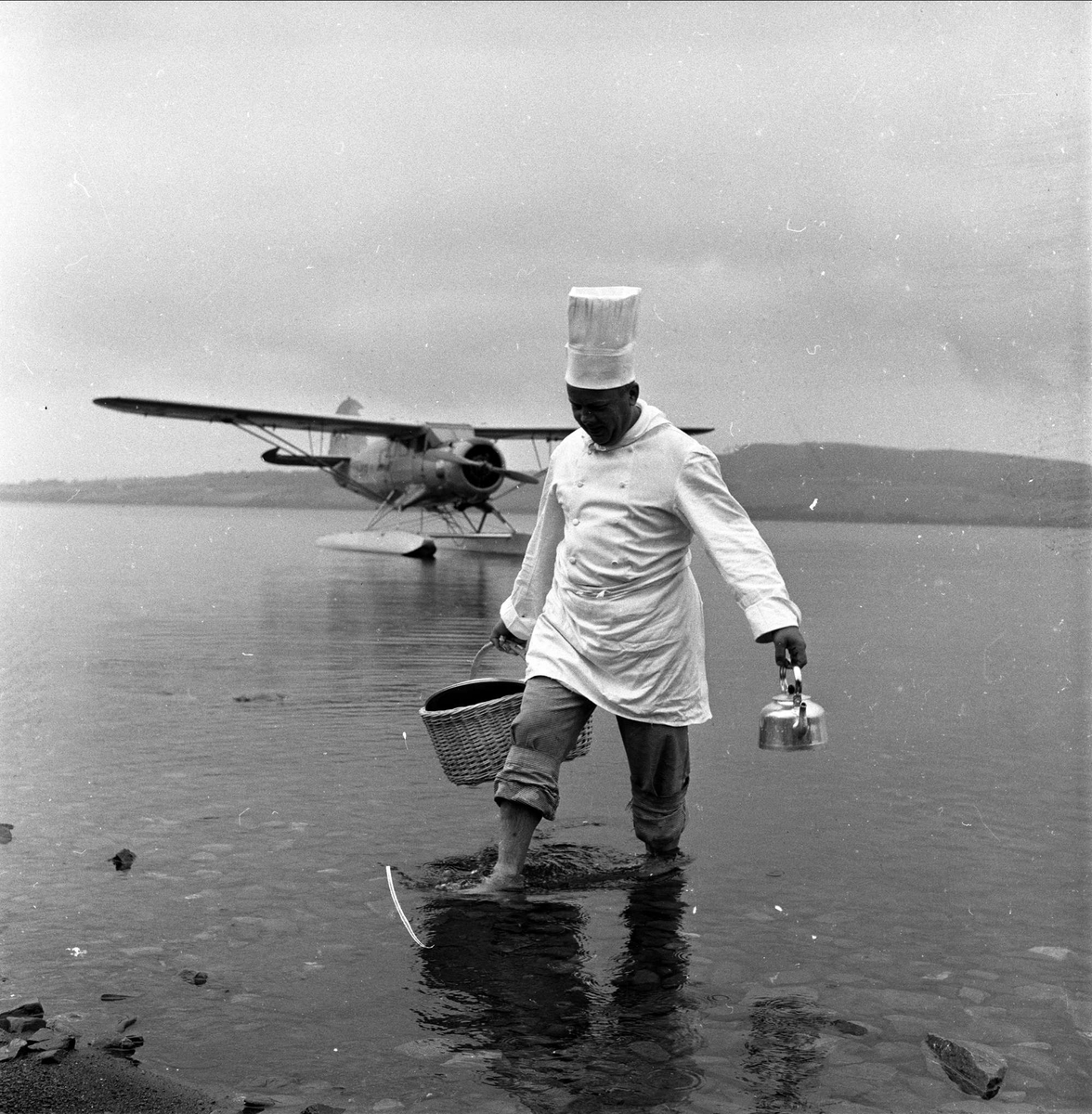 Mann på strand med sjøfly. Juli.1959. Dagblad frokost på Hamar.
