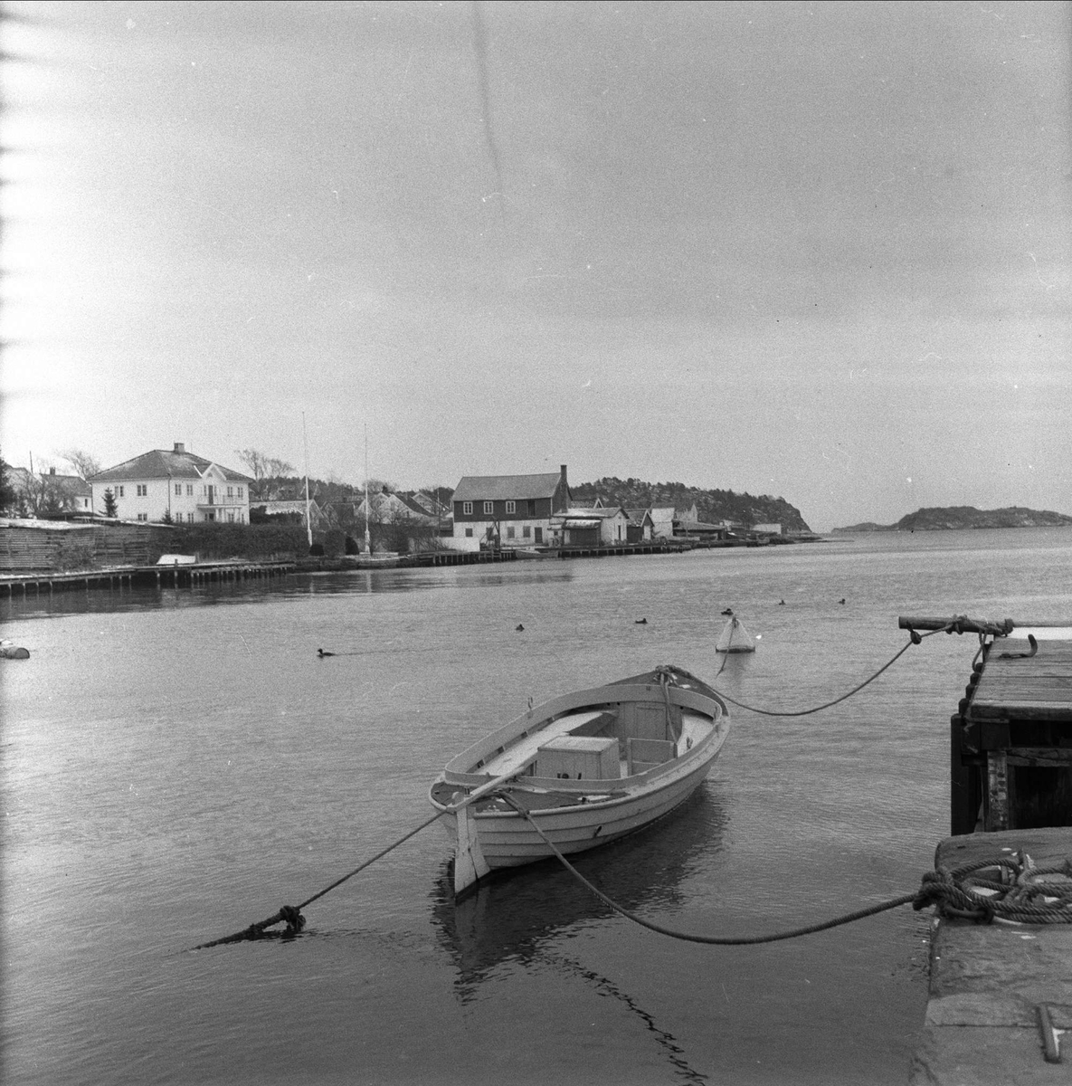 Lillesand, 02.12.1960. Trebåt ved brygge, bebyggelse i bakgrunnen.
